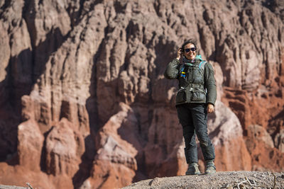 Woman in motorcycle gear, standing in front of red sandstone formation