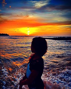 Silhouette boy standing on beach against sky during sunset