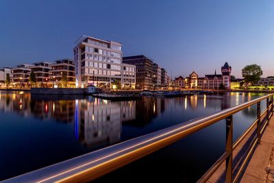 Illuminated buildings by river against sky at dusk