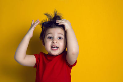 Cheerful baby boy in red t-shirt stands on yellow background