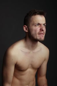 Portrait of young man looking away against black background