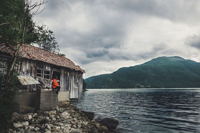 Woman in old building by lake against cloudy sky