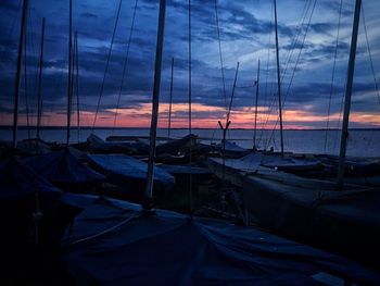 Sailboats moored at harbor against sky at sunset