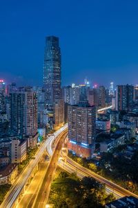 Aerial view of light trails on road amidst modern buildings against sky at night