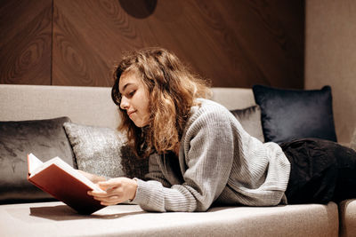 Teenager girl reading book on couch at home