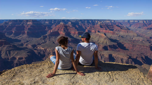 Rear view of friends sitting on rock against sky