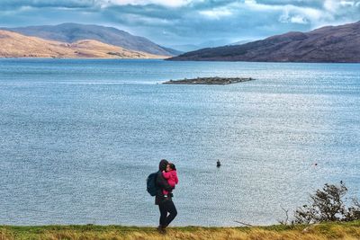Rear view of woman looking at lake against sky