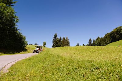 People riding motorcycle on field against clear blue sky