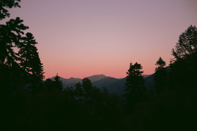 Silhouette trees by mountains against sky at sunset