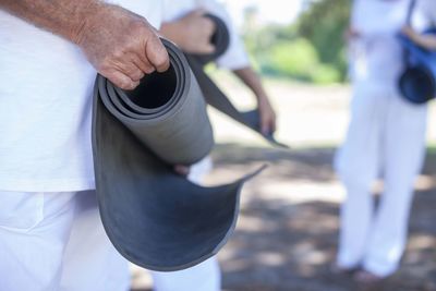 Elderly man rolling up fitness mat outdoors