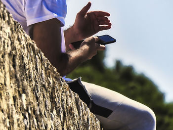 Midsection of man holding mobile phone against sky