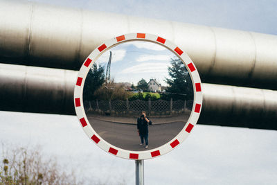 Reflection of man photographing with camera while standing on road against sky in road mirror