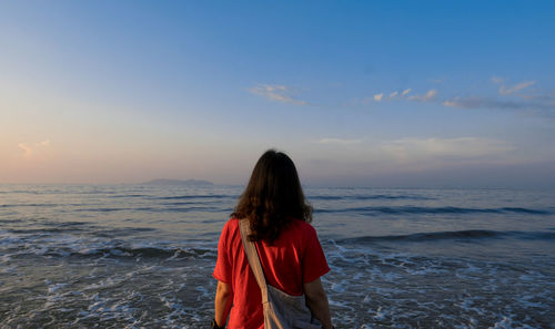 Rear view of woman standing at beach during sunset