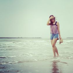 Young woman standing on beach against clear sky