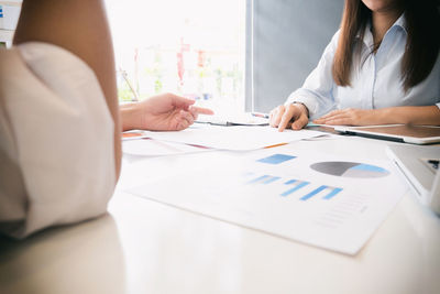 Midsection of business people discussing graphs on desk in office