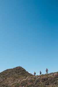 Rear view of man walking on mountain against clear blue sky