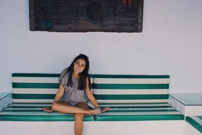 Portrait of smiling young woman sitting on couch against wall