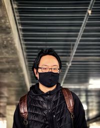 Portrait of young man in face mask standing against ceiling and wall.