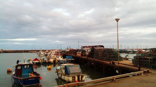 Boats moored at harbor against sky in city