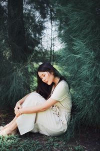 Beautiful young woman sitting on land against trees