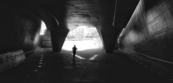 Silhouette man walking on footpath in tunnel