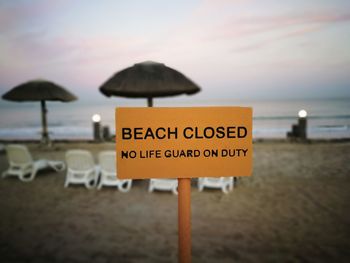 Close-up of information sign on beach against sky