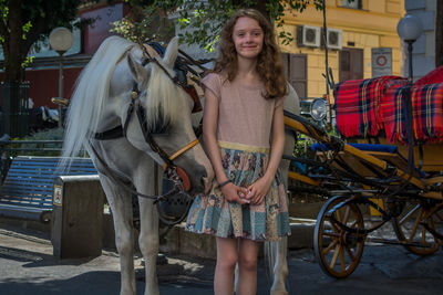 Portrait of smiling young woman standing by horse cart