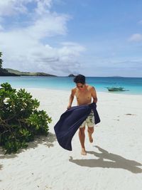 Full length of shirtless man walking at beach against sky