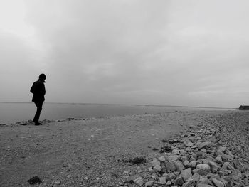 Rear view of man standing on beach against sky