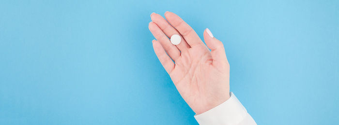 Close-up of person hand holding pill against blue background