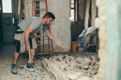 A young man breaks a brick wall with a sledgehammer.