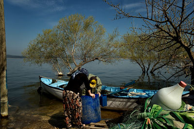 Rear view of man and woman looking into container by boat at lakeshore