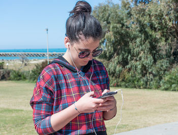 Young woman using mobile phone against trees