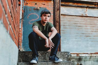 Portrait of teenage boy sitting on steps against wall