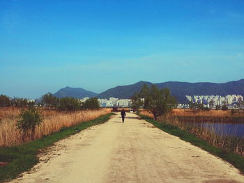 Country road leading towards mountains against blue sky