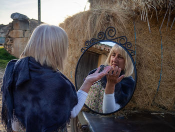 Reflection of woman gesturing in mirror by hay bales