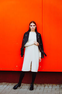 Portrait of young woman standing against red wall