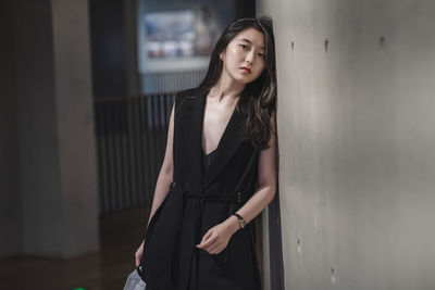 Beautiful young woman looking away while standing against wall