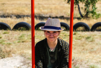 Smiling young woman in checkered shirt and hat swinging on swing on playground. hipsters and hippie 