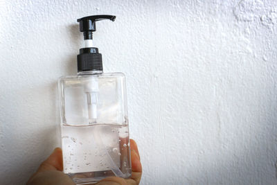 Close-up of hand holding bottle against wall
