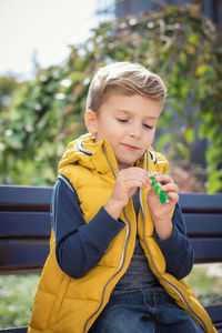 Boy holding candy while sitting on bench at park