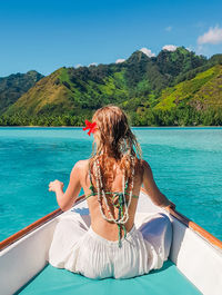 Rear view of woman sitting in boat on sea against blue sky