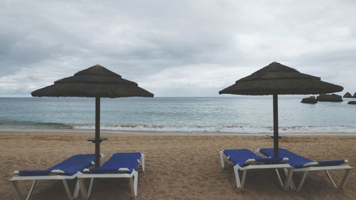 Deck chairs on beach by sea against sky