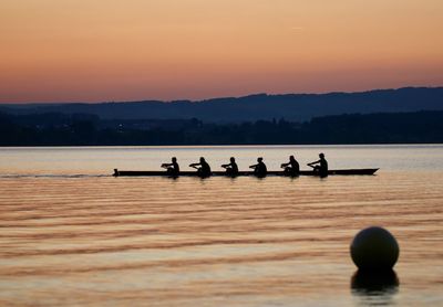 Silhouette people sailing in river against sky during sunset