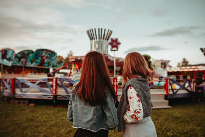 Rear view of women standing at amusement park against sky