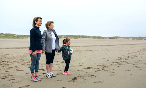 Woman standing with mother and daughter at beach against sky