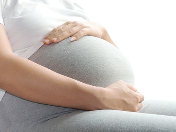 Midsection of pregnant woman with hands on stomach against white background