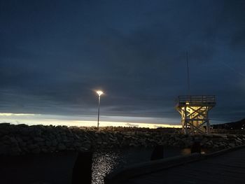 Illuminated built structure by sea against sky at night