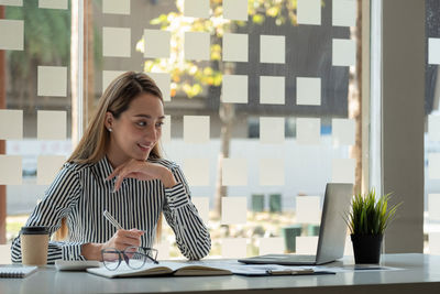 Portrait of young woman using mobile phone while sitting on table at home