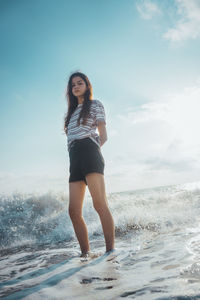 Full length portrait of young woman standing in sea against sky